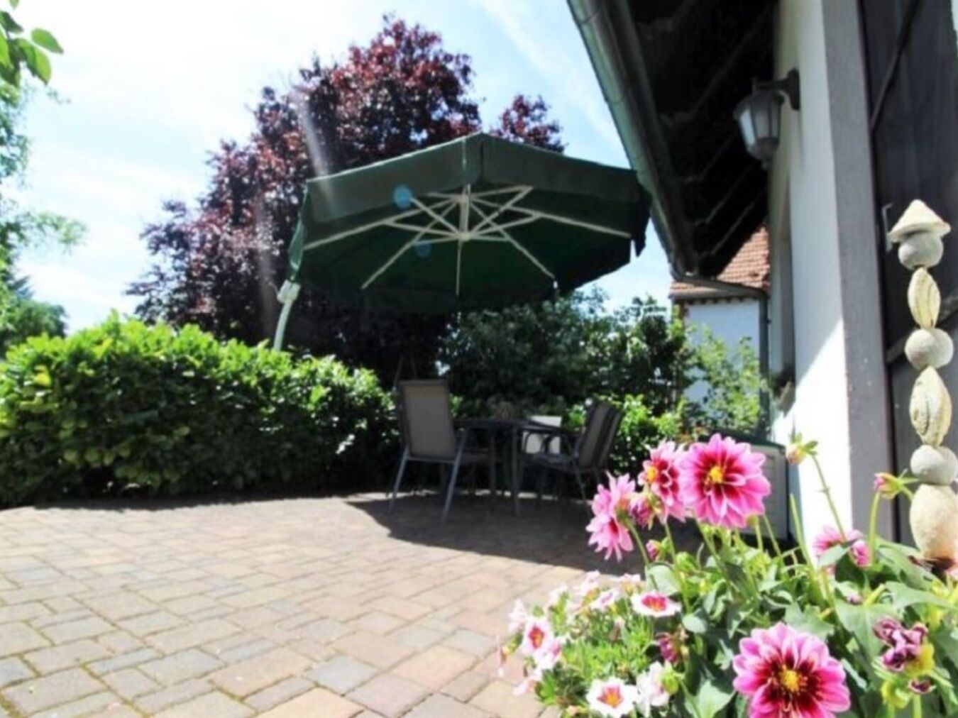 An outdoor patio area with a green umbrella, a table, and chairs.