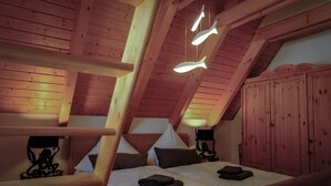 Une chambre confortable située dans les combles, avec un plafond en pente, des poutres en bois, un lit avec des oreillers et un luminaire suspendu.