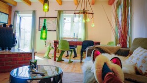 Un salon chaleureux avec un plafond en bois, une table basse en verre, un fauteuil vert, un canapé et un luminaire suspendu.