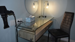 A bathroom with a glass vanity, a mirror, two wall-mounted lights, a hairdryer, and a chair.