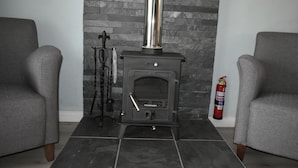 A room with a fireplace, two grey armchairs, a tiled floor, and a fire extinguisher.