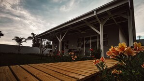 A modern house with a wooden deck, a covered porch, and a garden with flowers.