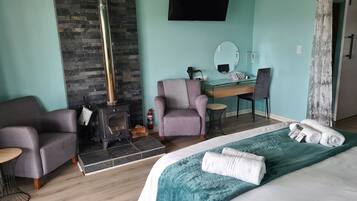 A modern hotel room with a stone fireplace, a desk with a mirror, a comfortable armchair, and a neatly made bed.