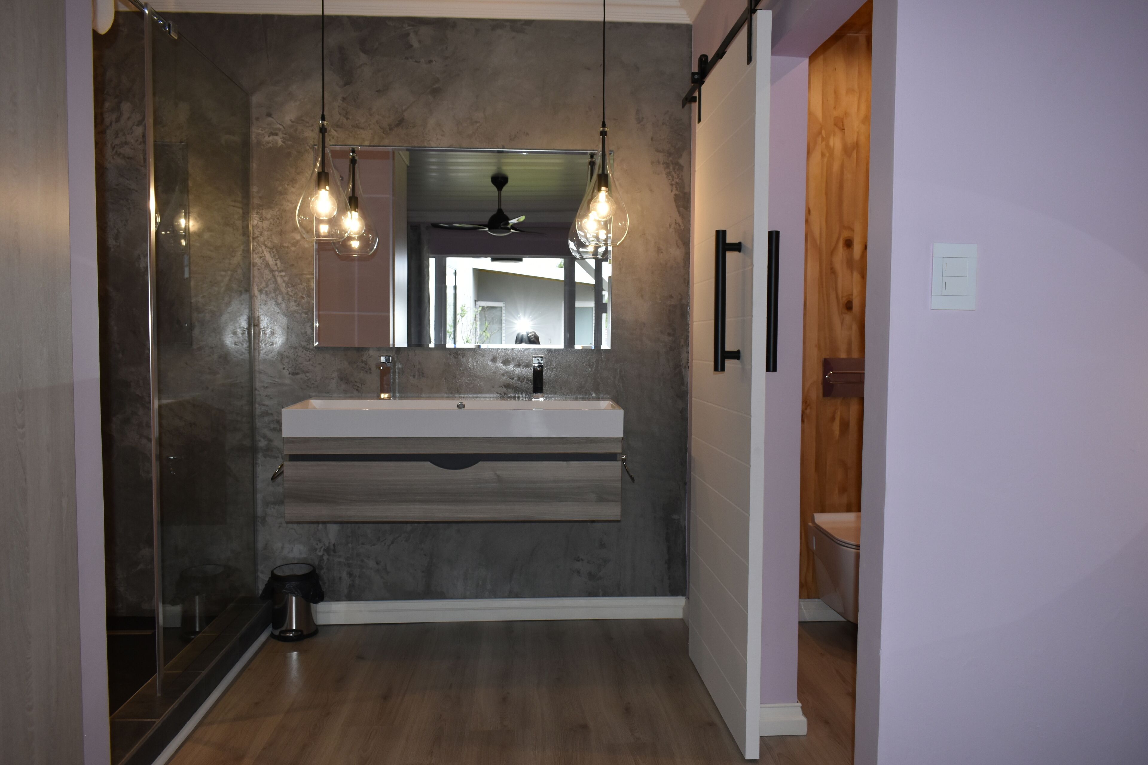 A modern bathroom with a large mirror, a built-in sink, and pendant lighting.