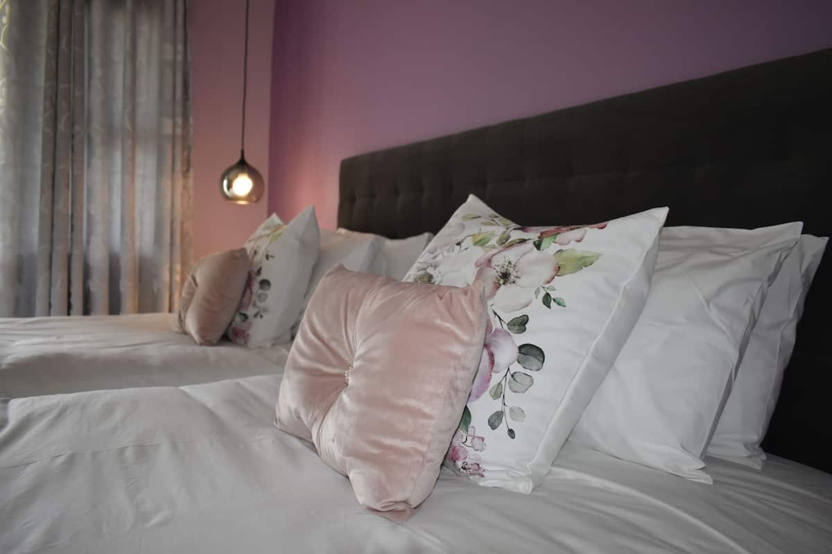 A neatly made bed with white linens and floral pillows, a dark headboard, and a hanging pendant light.