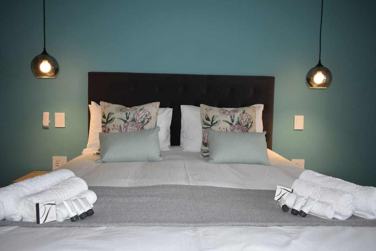 A neatly made bed with floral pillows, a grey rug, and white towels.