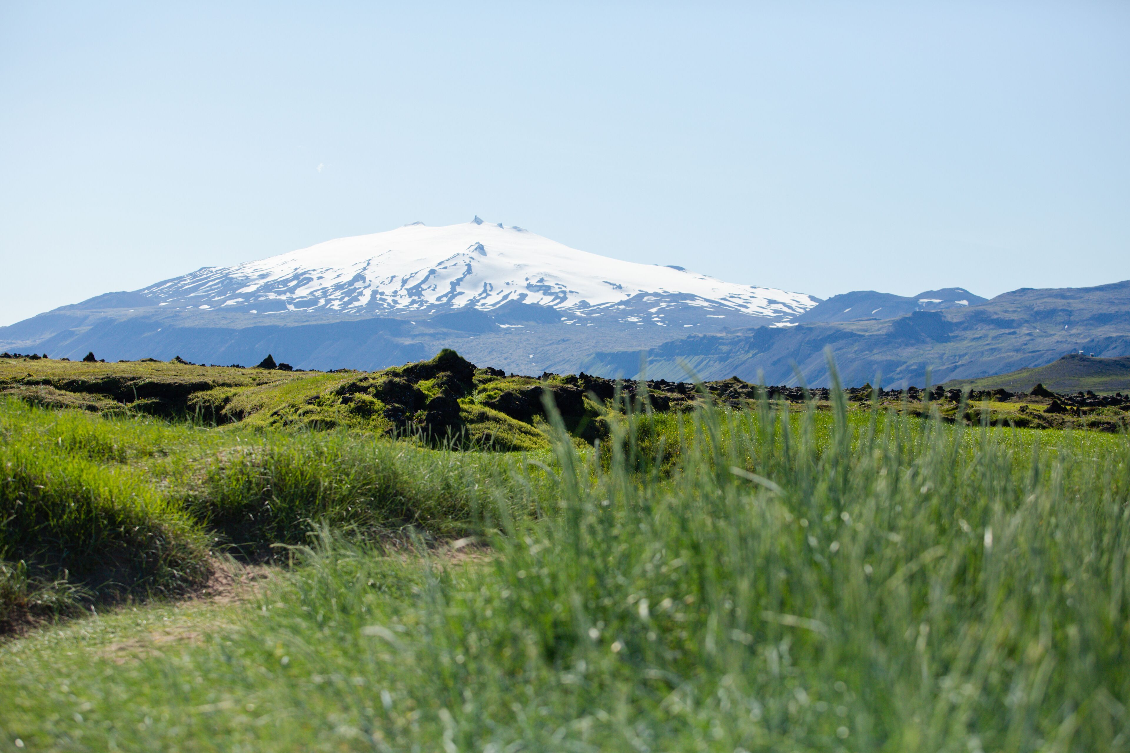 Ein Berg mit schneebedeckten Gipfeln, einem grasbewachsenen Vordergrund und felsigem Gelände.