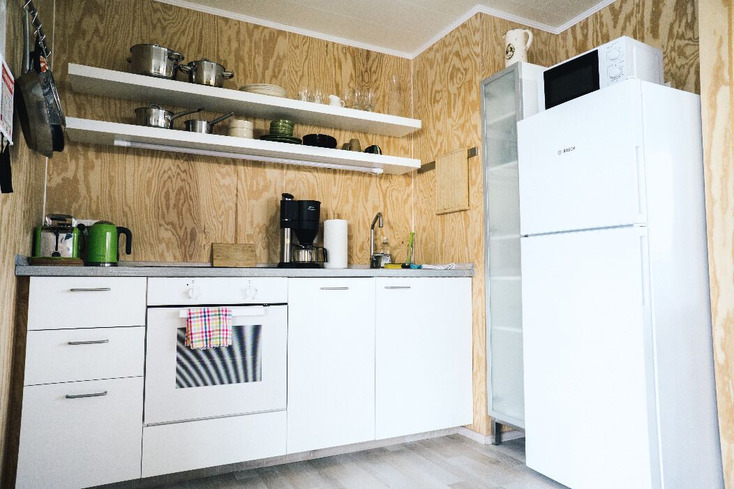 A compact kitchen with white cabinets, a built-in oven, a microwave, and wooden shelves above holding pots and pans.
