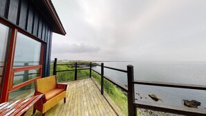 A wooden deck with a bench, overlooking a body of water and distant land.