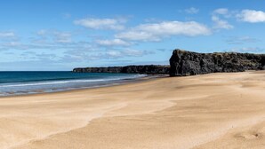 A beach with a rocky outcrop and calm sea.
