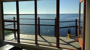 A large window with a view of the sea and a wooden deck.