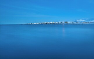 A coastal town with buildings along the shore, a clear sky, and calm sea.