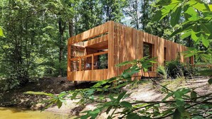 Une cabane en bois dotée d’un balcon, entourée d’arbres et bordée par un plan d’eau.