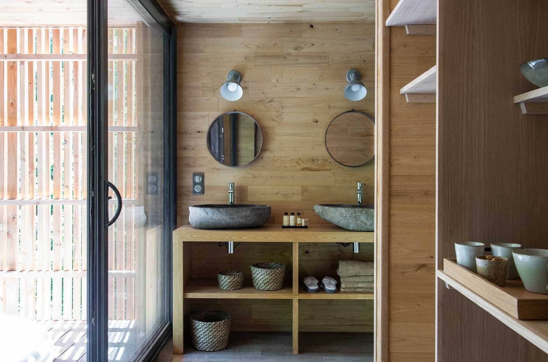 Une salle de bain moderne avec des murs en bois, deux miroirs ronds et un lavabo central.