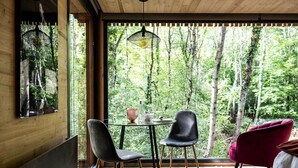 Une pièce dotée d’une grande fenêtre donnant sur la forêt, d’une table ronde entourée de chaises et d’un luminaire suspendu.