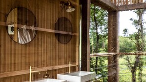 Une salle de bain moderne avec deux lavabos, des murs en bois et une grande fenêtre donnant sur une forêt.