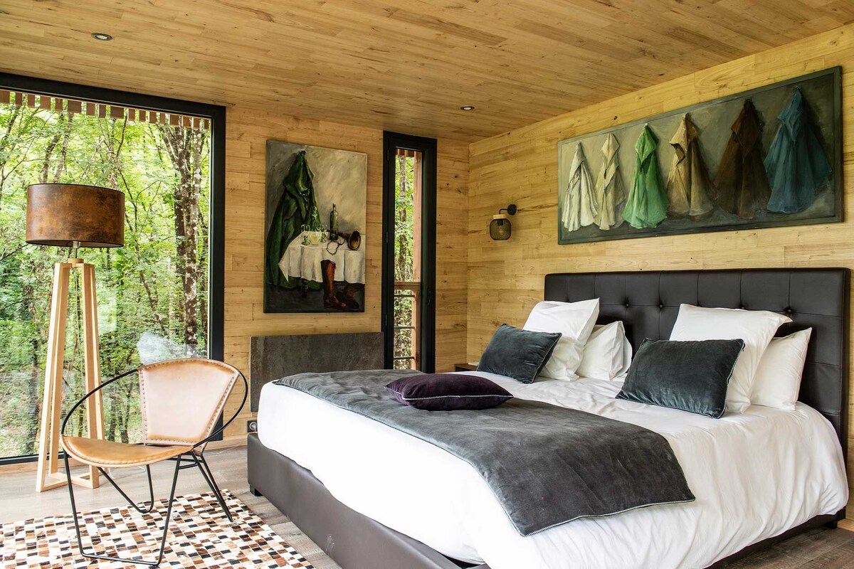 A bedroom with a large bed, a chair, a painting, and a lamp.