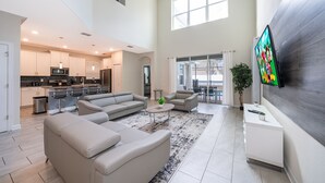 A spacious living area with a large sofa set, a coffee table, and a flat-screen TV mounted on the wall.