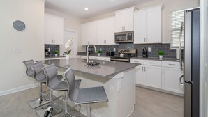 A modern kitchen with white cabinets, a stainless steel refrigerator, and a central island with bar stools.