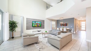 A modern living room with a flat-screen TV, two sofas, a coffee table, and a dining area with a table and chairs.