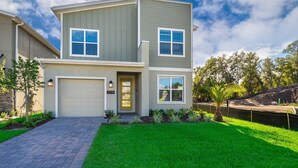 A two-story house with a garage, a well-maintained lawn, and a small pond.