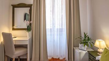 A hotel room with a bed, a desk, a chair, a lamp, and a window with curtains.