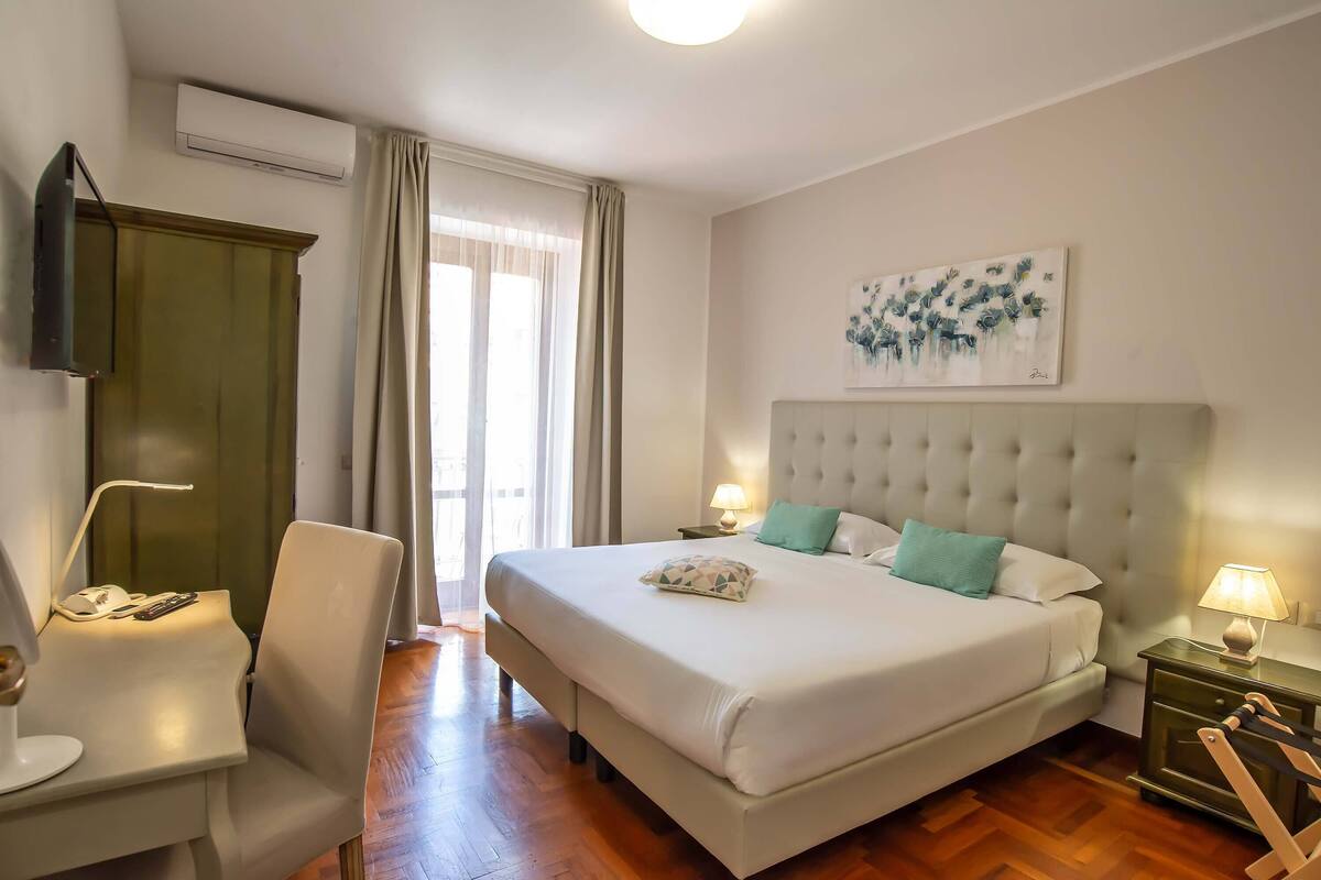 A hotel room with a large bed, a desk with a chair, a TV, and a painting on the wall.