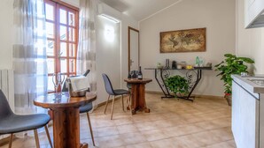 A dining area with a wooden table, two chairs, a wine glass, and a bottle. There is a window with curtains, a map on the wall, and a plant on a table. - Plaza Rooms Ciampino (Ciampino)