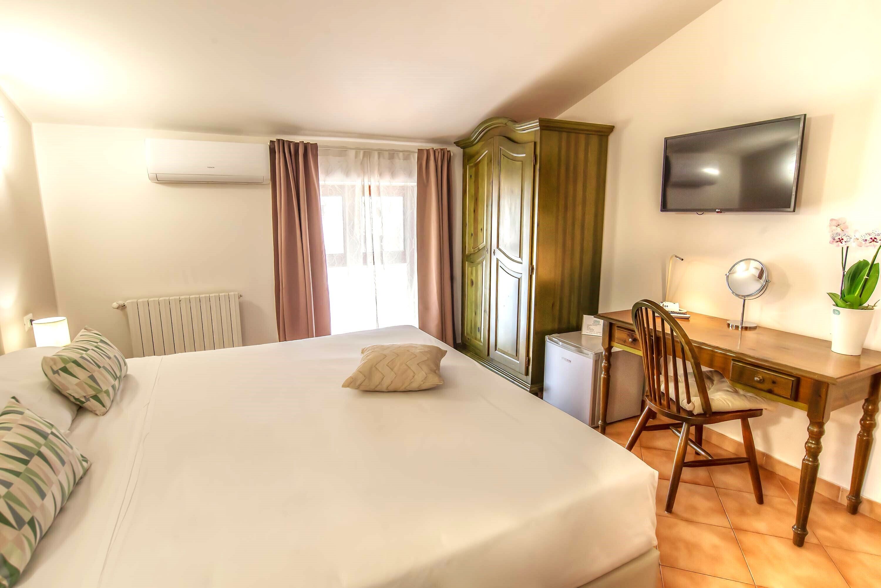 A hotel room with a bed, a desk, a chair, a television, and a radiator.