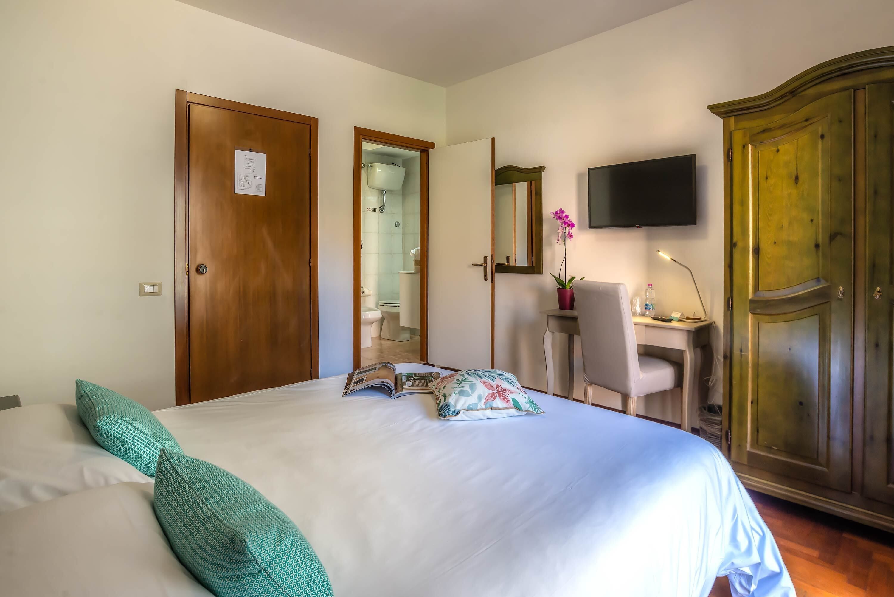 Una habitación de hotel con cama, escritorio, televisor y armario.