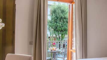 Habitación de hotel con balcón, una mesa de comedor con sillas y vistas a un árbol y cactus.
