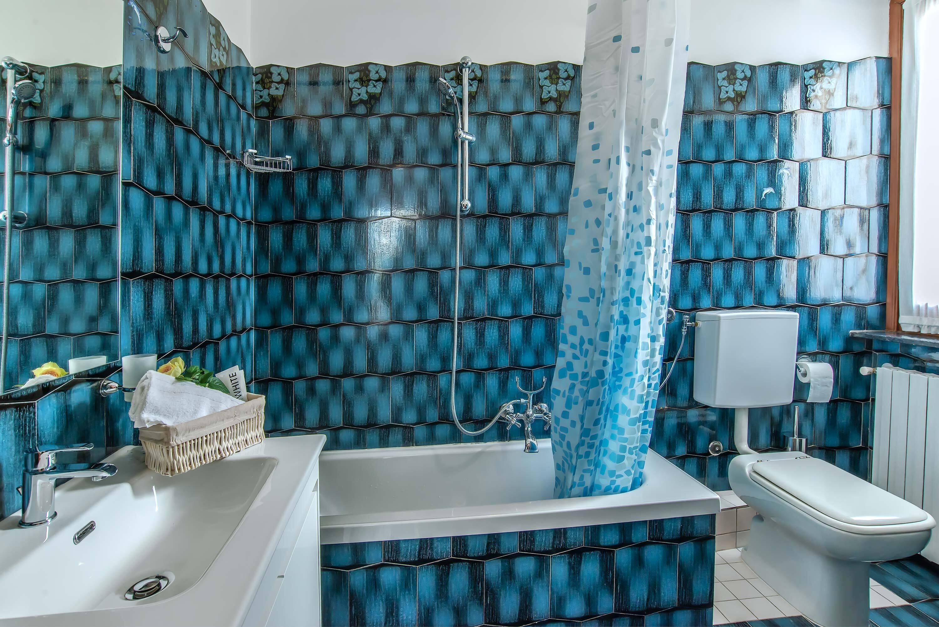 Une salle de bain équipée d’une baignoire, de toilettes et d’un espace douche, avec des carreaux bleus à motifs.