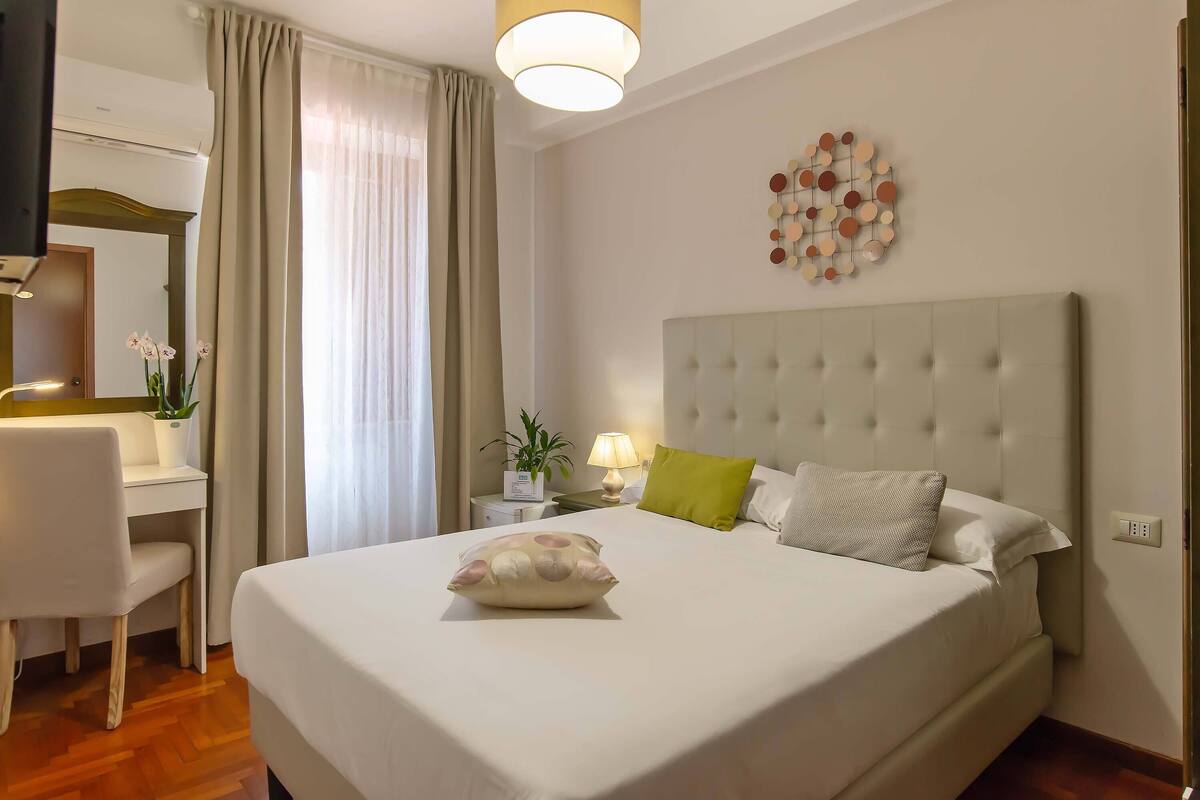 A hotel room with a large bed, a desk, a chair, a lamp, and a wall decoration.