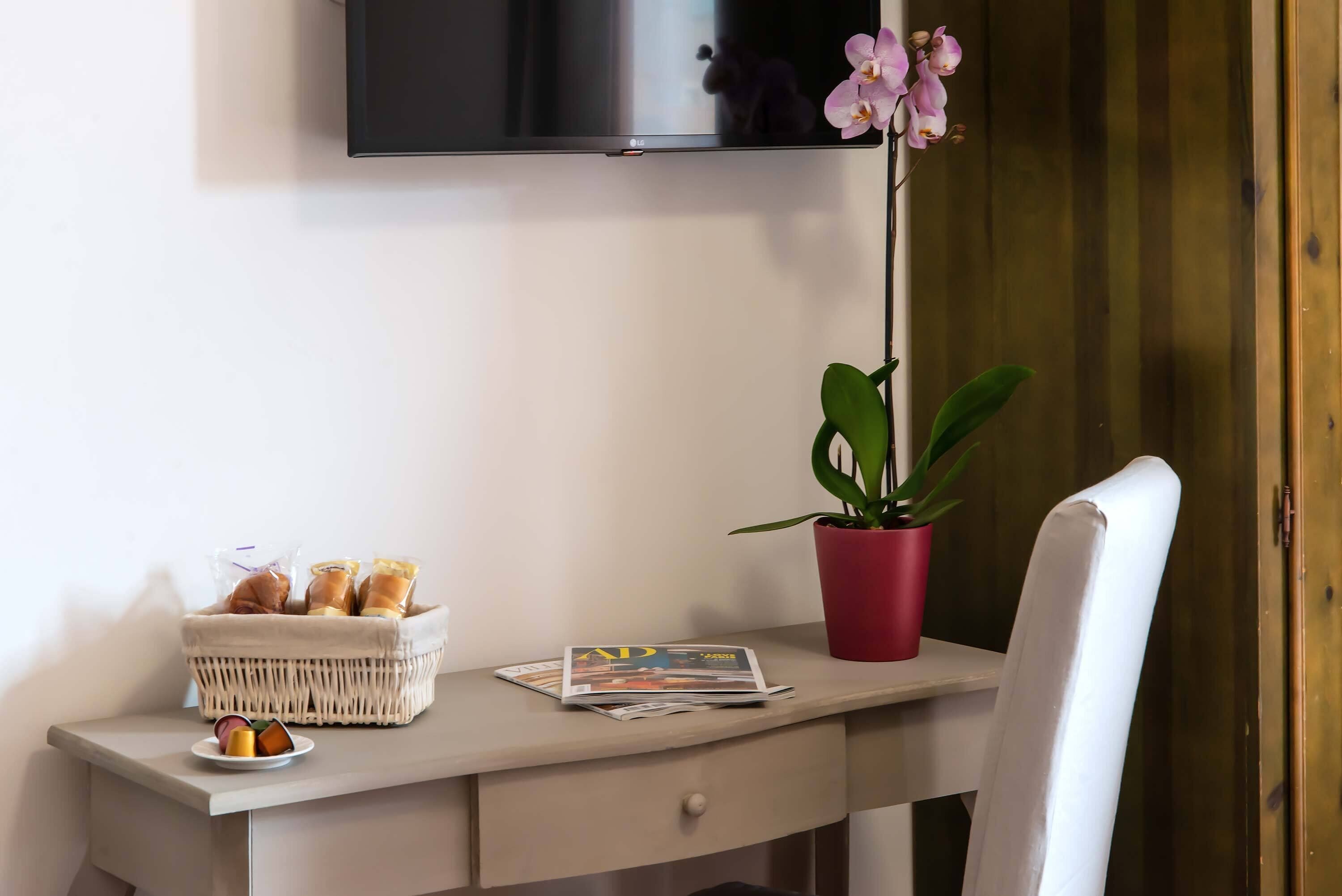 A desk with a basket of pastries, a plate with fruit, a magazine, and a potted plant.