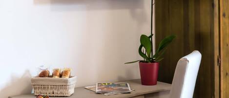 A desk with a basket of pastries, a plate with fruit, a magazine, and a potted plant.