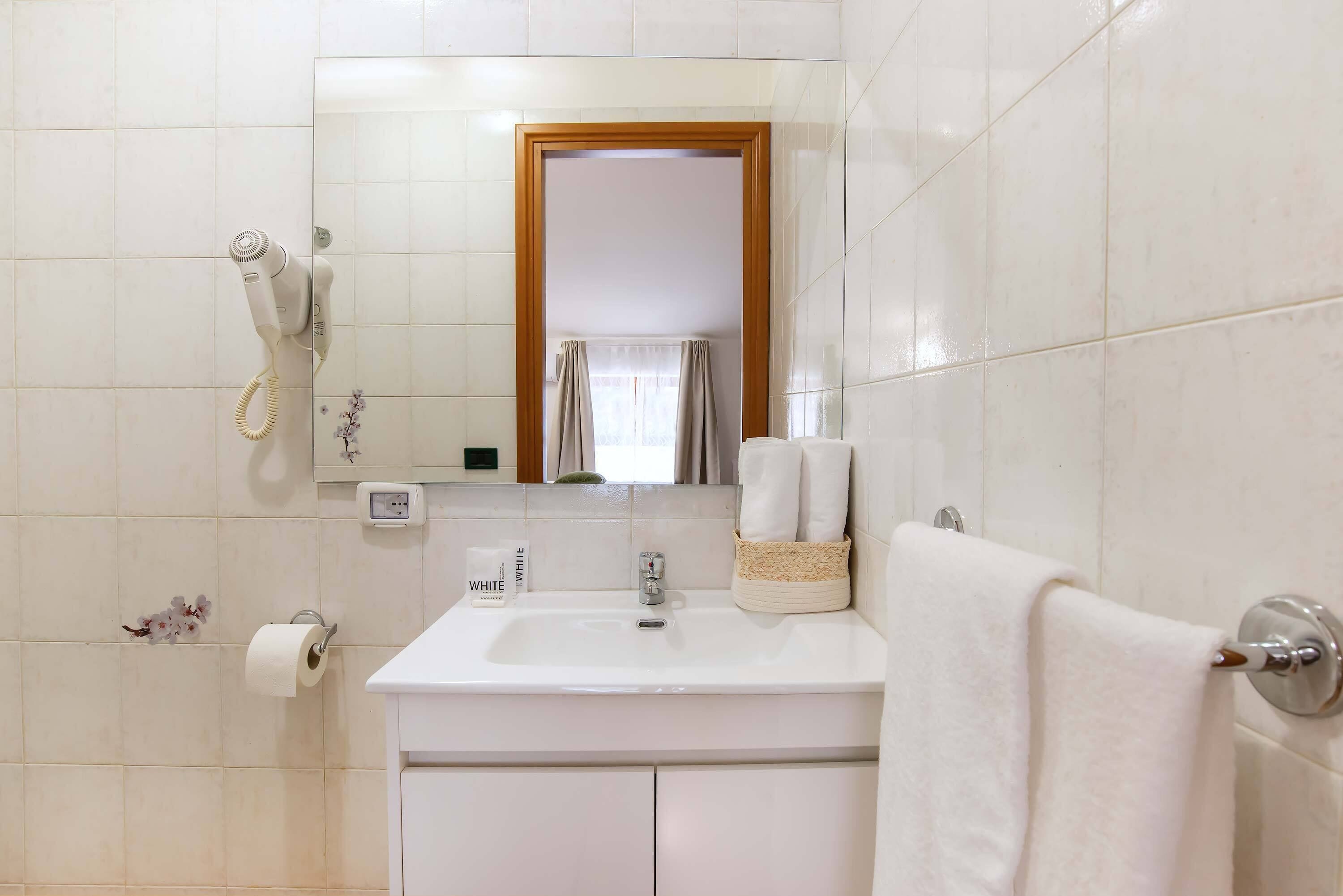 A bathroom with a white sink, a mirror, a hairdryer, a towel rack, and a toilet paper holder.