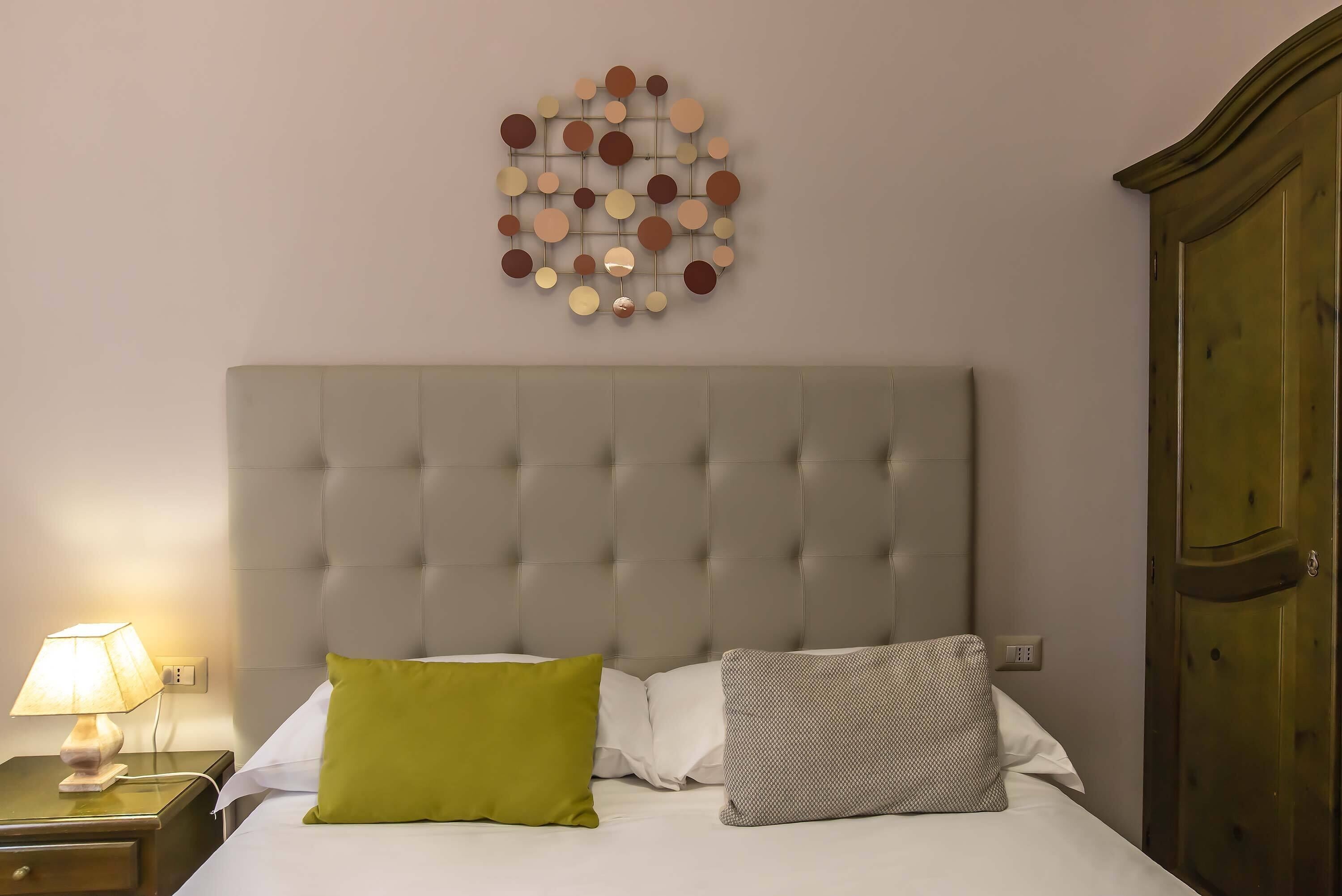 A neatly arranged bedroom with a tufted headboard, a bedside table with a lamp, and two pillows on the bed.