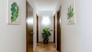 A hallway with two doors on either side, a potted plant in the center, and artwork on the walls. - Plaza Rooms Ciampino (Ciampino)