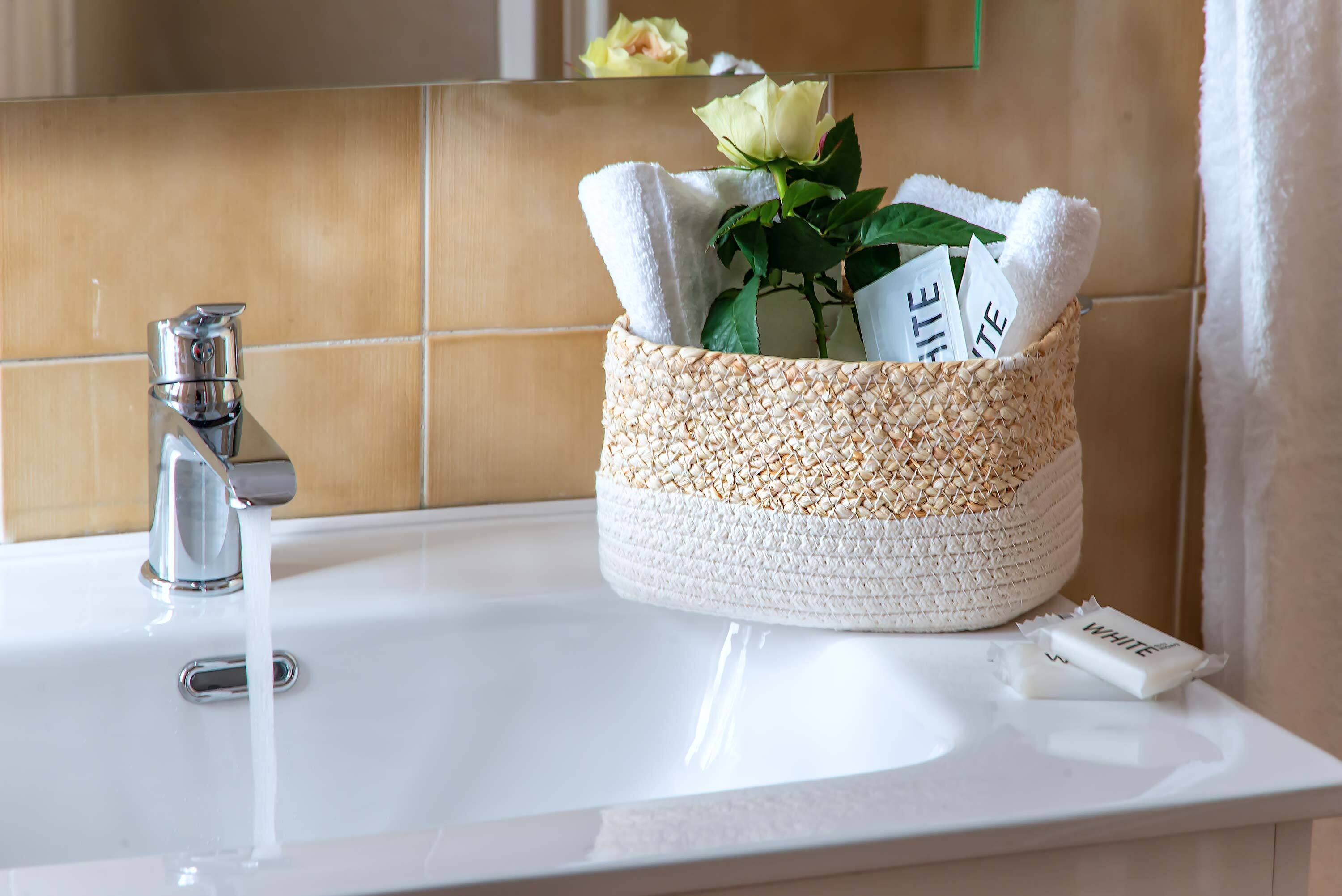 A bathroom sink with a woven basket containing towels and a rose.