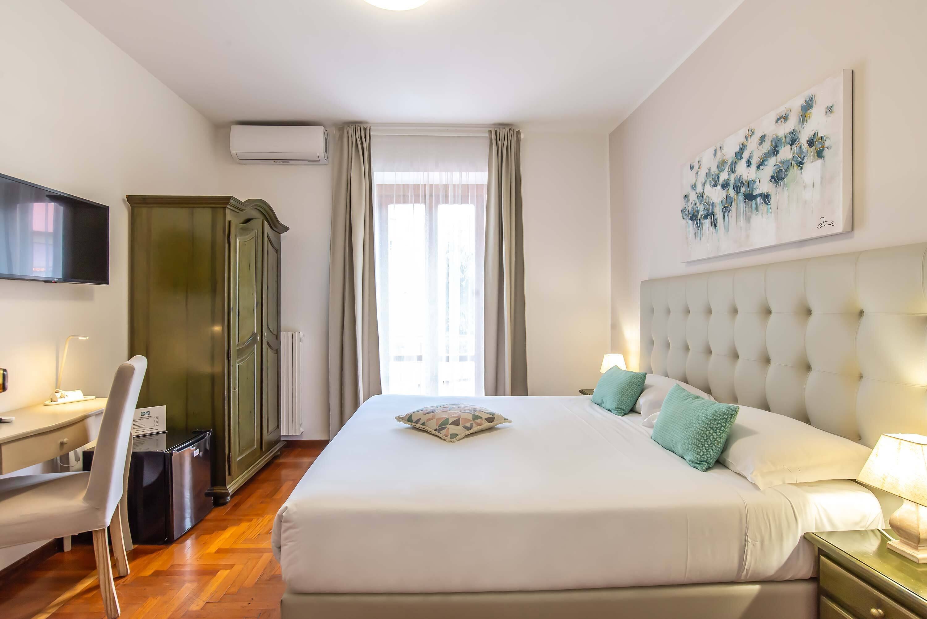 Une chambre d’hôtel avec un lit, un bureau, une chaise, une armoire et un tableau au mur.