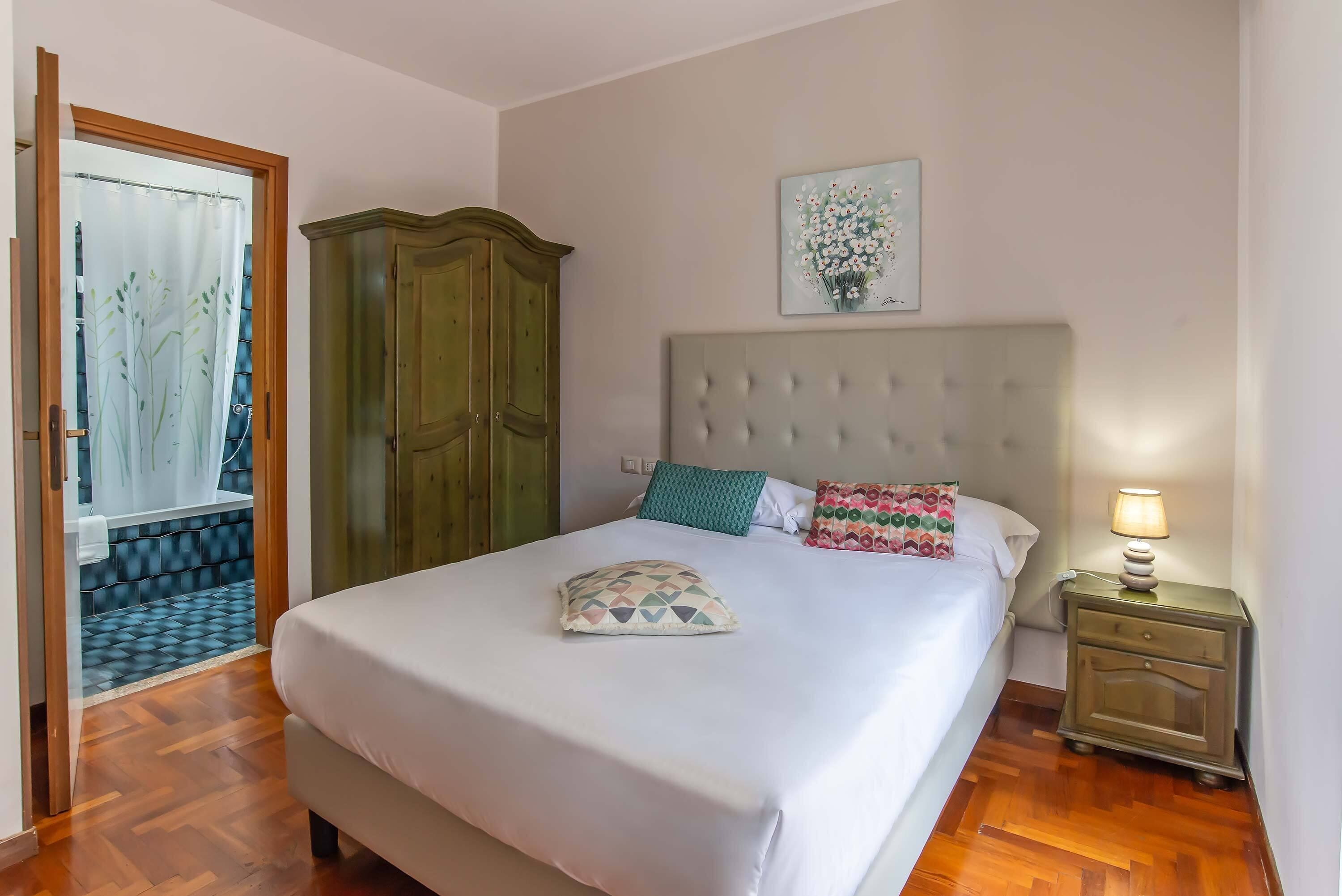 A neatly made bed with a patterned pillow, a green headboard, and a bedside table with a lamp.