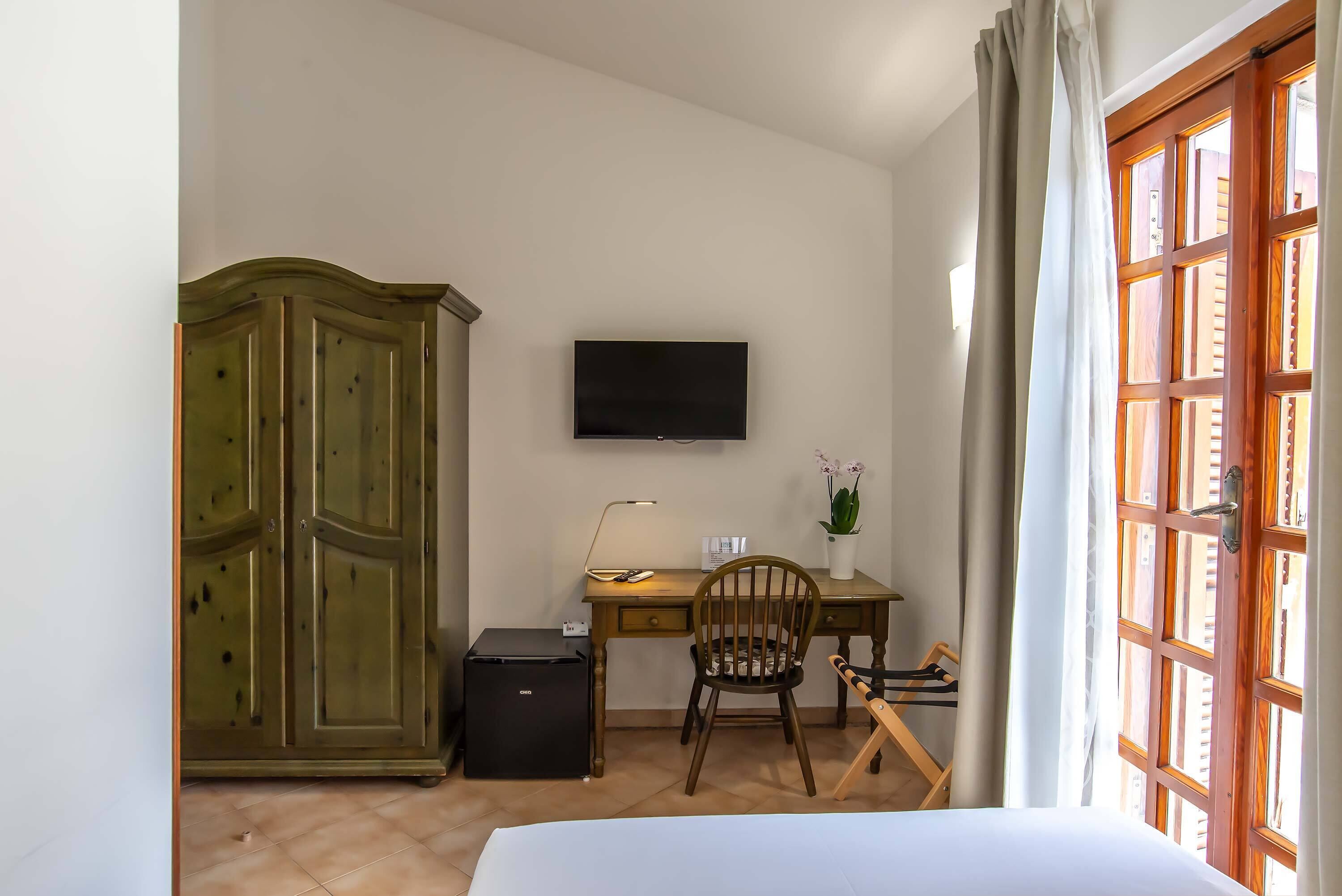 Ein Zimmer mit Bett, Schreibtisch mit Stuhl, Fernseher, Kleiderschrank und einem Fenster mit Vorhängen.