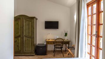 Ein Zimmer mit Bett, Schreibtisch mit Stuhl, Fernseher, Kleiderschrank und einem Fenster mit Vorhängen.