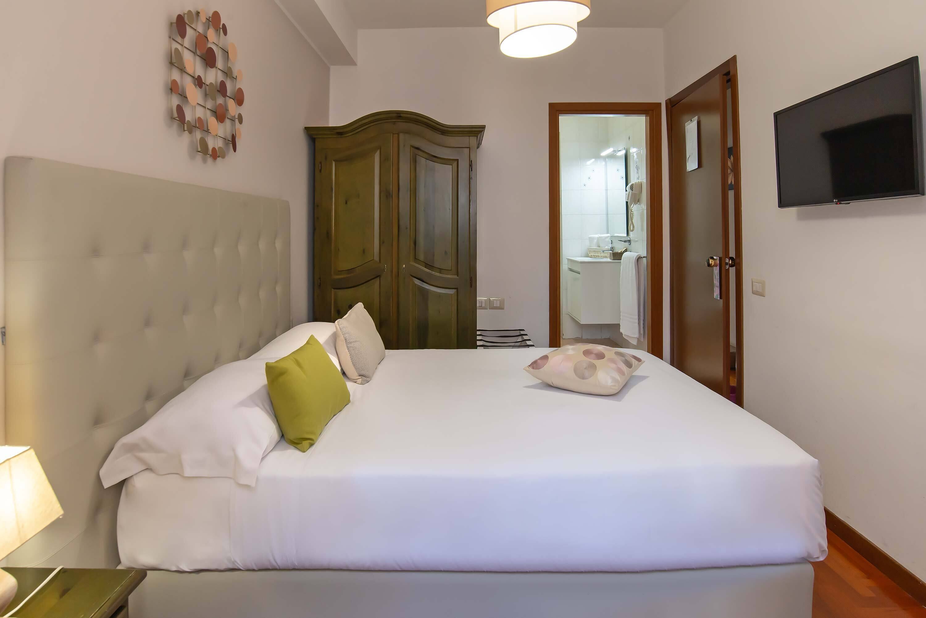 A bedroom with a large bed, a wardrobe, a television, and a bathroom visible through an open door.