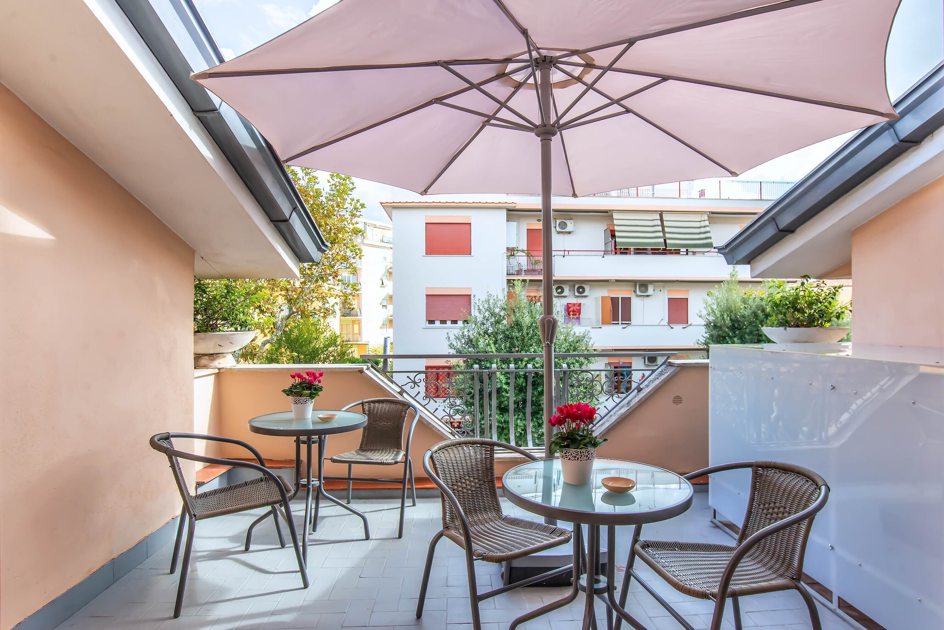 A balcony with wicker chairs, a glass table, and a large umbrella.