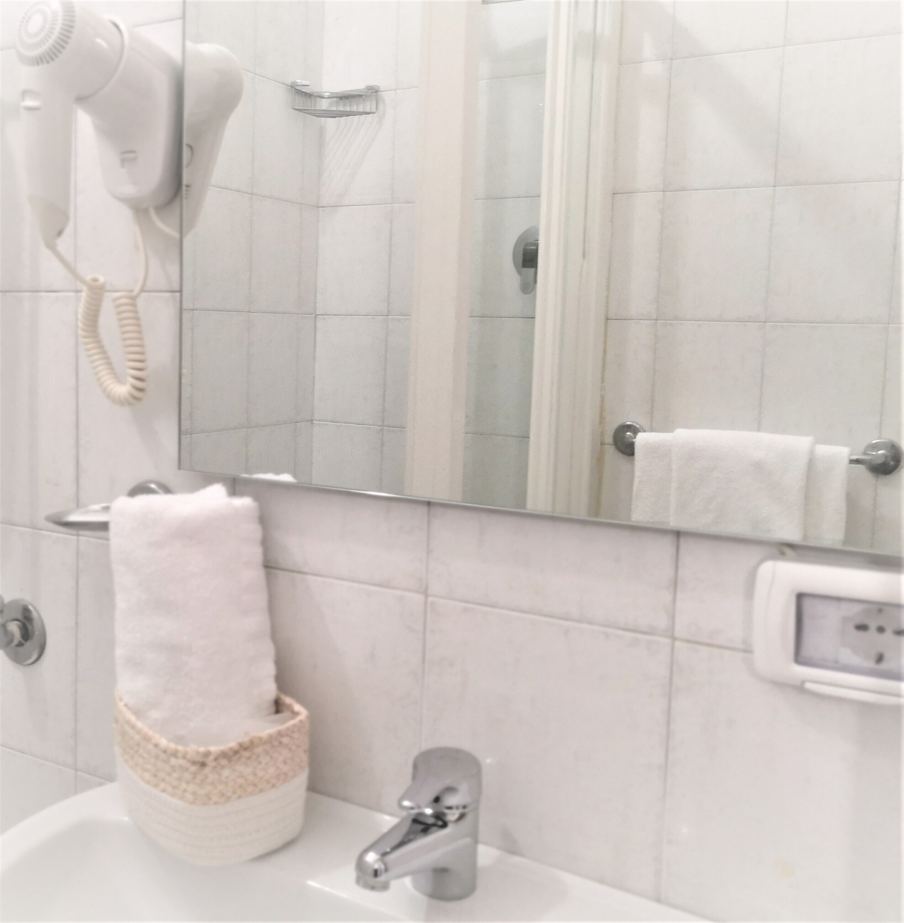 Ein Badezimmer mit Waschbecken, Spiegel, Föhn und Handtuchhalter.