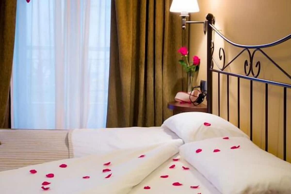 A hotel room with a bed, a bedside table with a lamp, and a window with curtains.