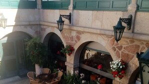 An outdoor patio area with stone walls, green window frames, and a fountain. There are wicker chairs and tables arranged for dining. - Hotel Fonte da Vila (Monção)