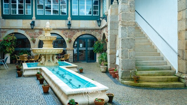 A courtyard with a fountain, outdoor seating, and a staircase leading to a building with a sign reading "Restaurante". - Hotel Fonte da Vila (Monção)