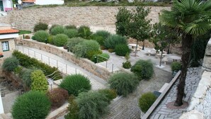 A landscaped garden with various shrubs and trees, a stone wall, and a paved walkway. - Hotel Fonte da Vila (Monção)